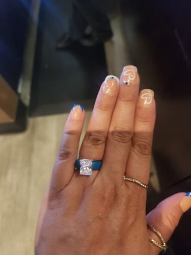 A reviewer's hand wearing the blue Silicone Ring with a large, emerald-cut CZ.