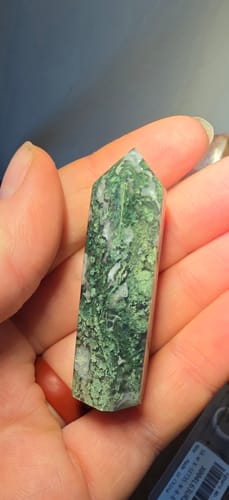 Customer holding a pointed, green and white crystal from the monthly program in their palm.