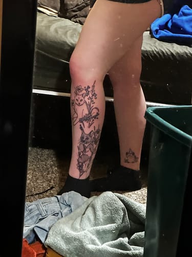 Reviewer showing the finished line work of a large cat and flower tattoo on their shin after using the numbing cream.