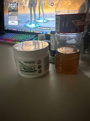 Customer's white tub of D-BLOAT powder on a desk next to a computer and a bottle of liquid.