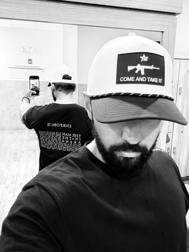 Reviewer's mirror selfie in a gym showing the back text design on the black Man in The Arena Tee.