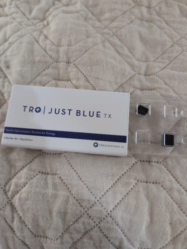 Customer shows the Just Blue box next to a blister pack with two dark, square troches on a quilted surface.