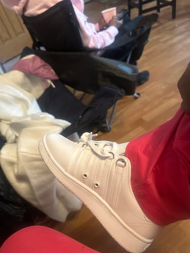 Reviewer lifting their foot to show a side view of the white CLASSIC VN sneaker against a wooden floor.