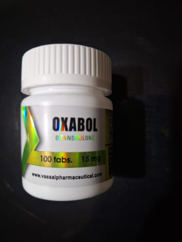 Cliente muestra el frasco blanco de Oxabol (Oxandrolona) de 15 mg y 100 tabletas sobre una superficie oscura.