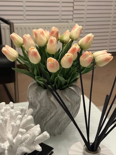 Recensent toont het oud roze tulpenboeket met gesloten knoppen in een vaas op een salontafel.