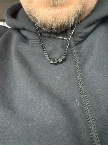 Close-up of a reviewer wearing the black chain Legacy Set necklace against a black hoodie.