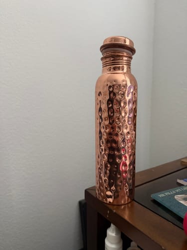 Customer's hand-hammered pure copper water bottle standing upright on a wooden surface.