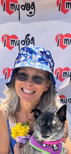 Reviewer smiling while wearing the Carrot And Rabbit Pattern Print Bucket Hat and holding a small dog.
