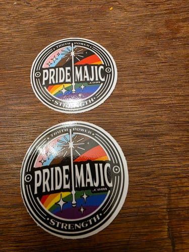 Customer's two circular stickers of different sizes with a colorful 'Pride Majic' design on a wooden surface.