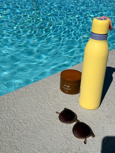 Customer's Intensive Tanning Balm in its brown jar, sitting by a sunny swimming pool.