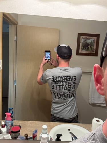 Reviewer taking a mirror selfie showing the back of a gray graphic t-shirt with a message about kindness.