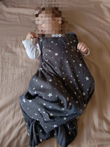 Customer's baby lying down while wearing the gray, star-patterned Ultimate Baby Sleep Bag.