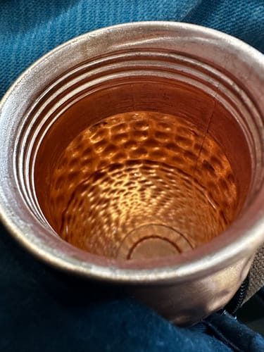 Close-up of the reviewer's copper water bottle, showing the hammered interior and dark screw threads at the opening.