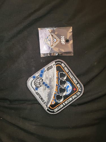 Customer's embroidered Artemis II - Collectors Patch and a matching pin on a black fabric background.