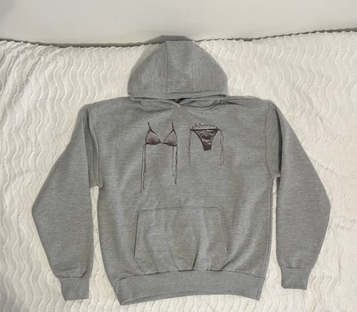 Customer's air dry grey hoodie with a bikini graphic laid flat on a white textured surface.