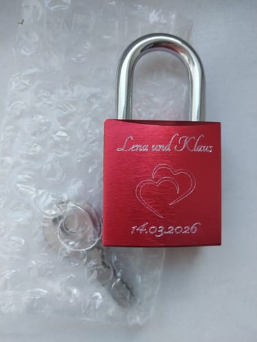 Rezensent zeigt das rote Liebesschloss mit der Gravur 'Lena und Klaus', zwei Herzen und Datum.