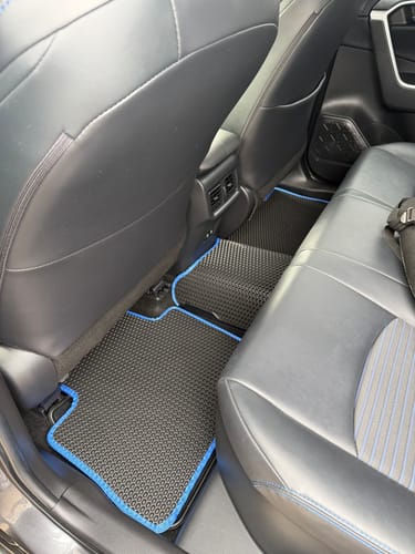 Recenzent pokazuje czarne dywaniki samochodowe z niebieską lamówką, dopasowane do podłogi w tylnej części samochodu.