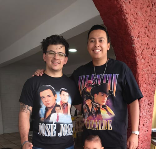 Un cliente sonriente posando con su camiseta negra de José José junto a otra persona.