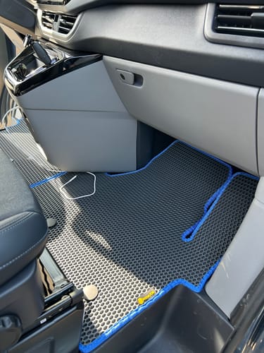 Klient pokazuje czarne dywaniki samochodowe z niebieskim obszyciem, idealnie dopasowane do wnętrza vana.