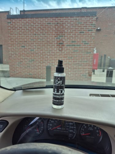 A reviewer's bottle of LUX Spray Scent sitting on their car dashboard.
