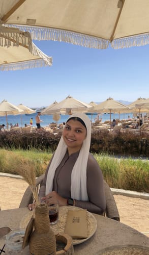 Reviewer smiling at a beachside table wearing the brown Sofia Shimmer bodysuit top.