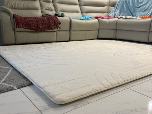 Customer's plush, cream Mellow Mat laid on a tiled living room floor in front of a sofa.
