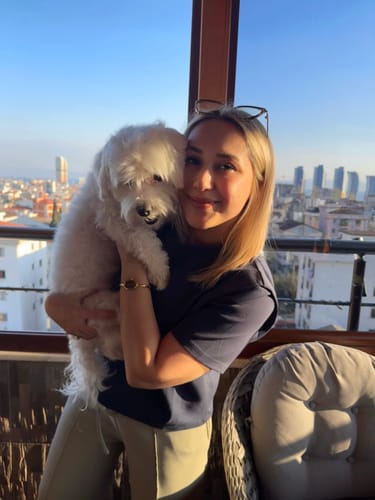 Customer wearing the stylish Diana Gold Brown watch on her wrist while holding a fluffy white dog on a balcony.