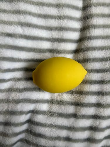 Reviewer's yellow Lem Clitoral Massager resting on a striped grey and white blanket.