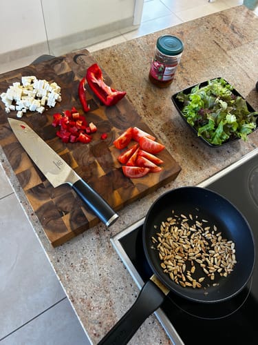 Rezensent zeigt ein Premium Küchenmesser aus der Mystery Box bei der Zubereitung eines Salats auf einem Holzbrett.