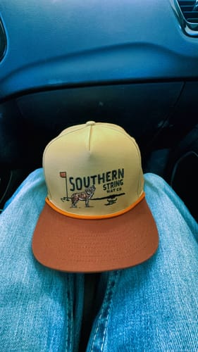 Customer's tan and brown Southern String trucker hat resting on their lap inside a car.