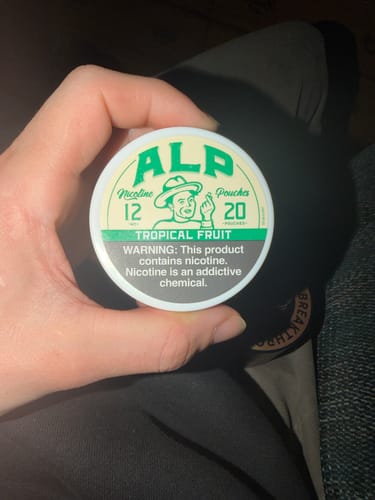 Customer holding a round, white can of ALP Tropical Fruit Nicotine Pouches.