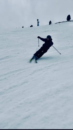 Customer skiing down a snowy slope wearing the black baggy Oxford workwear snow pants.