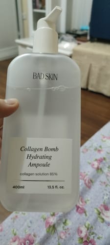 Reviewer holding a large, translucent bottle of Bad Skin Collagen Bomb Hydrating Ampoule.