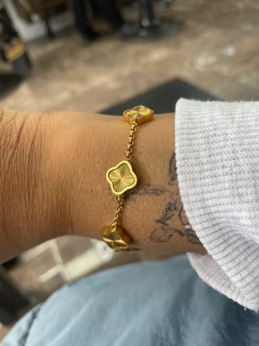 Reviewer wearing a gold-colored bracelet with textured clover charms on their wrist.