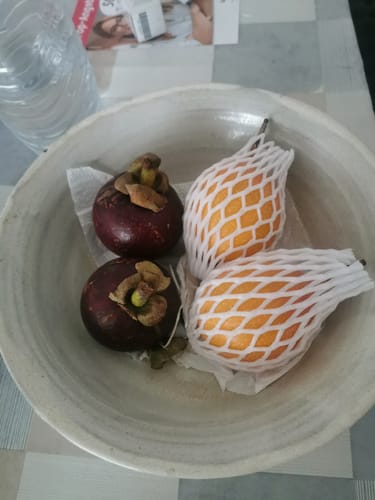 Ein Kunde zeigt zwei lila Mangostans und zwei gelbe Granadillas in einer hellen Schale.