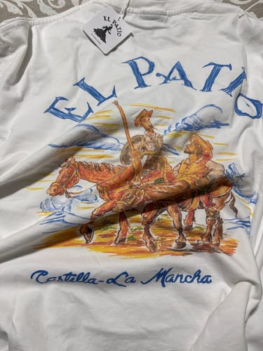 Customer's white La Camiseta: Quixote t-shirt laid out, showing the colorful graphic of Don Quixote and Sancho Panza.