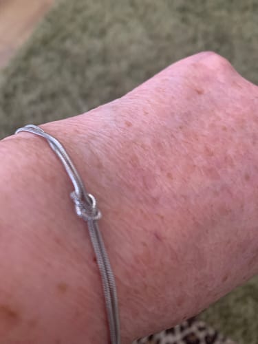 Close-up of a reviewer wearing a thin silver bracelet with a knot design.