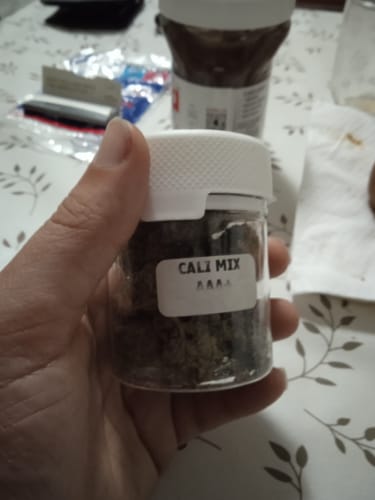 Customer's hand holding a small clear jar filled with CALI MIX AAA+.