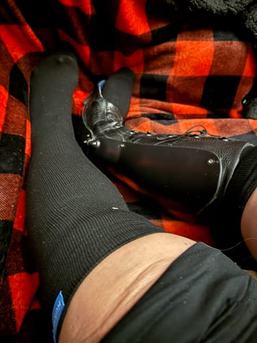 Close-up of a customer wearing a black Performance Eucalyptus Compression Sock on one leg while resting.