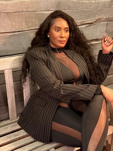 Reviewer wearing the open Pinstripe Suited Blazer over a black top while sitting on a wooden bench.