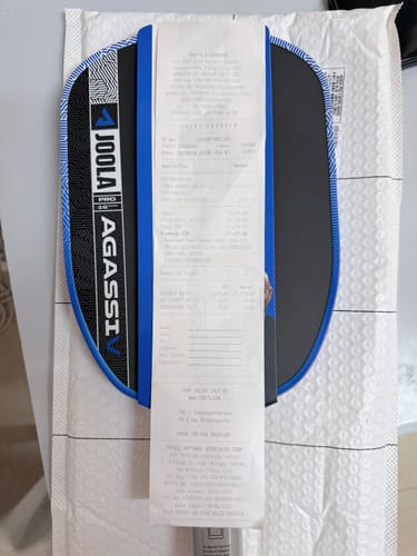 Reviewer shows the incorrect JOOLA Agassi V paddle received, partially covered by a long receipt.