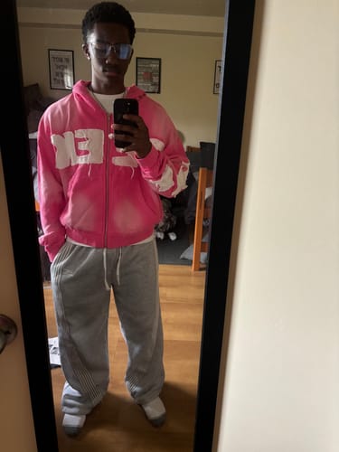 Reviewer in a mirror selfie wearing the pink SEEK ZIPUP hoodie with distressed white lettering.