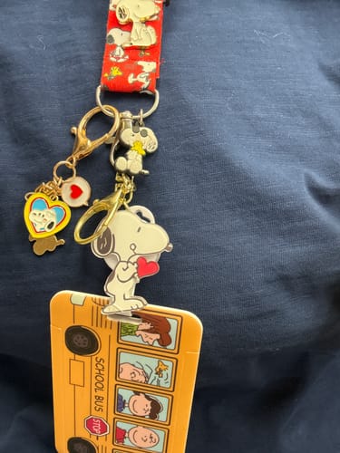 Customer showing Snoopy items from a mystery box, including a red lanyard, keychains, and a school bus ID holder.