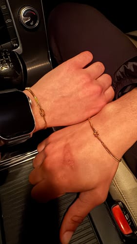 A customer shows two wrists, each wearing a matching golden Forever Knot Bracelet.