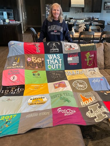 Customer stands behind her colorful Project Repat T-Shirt Quilt, which is spread out over the back of a sofa.