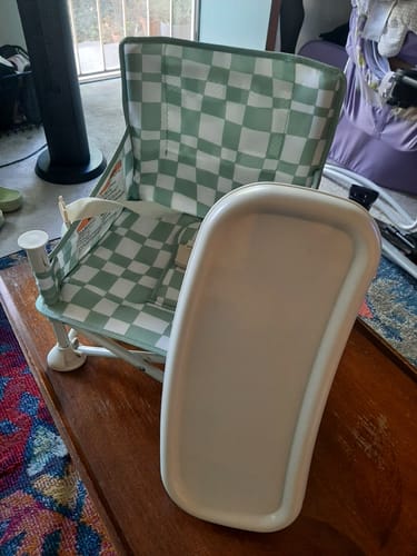 Reviewer's Parker portable booster chair with a green checkered pattern, showing the detached white tray next to it on a table.