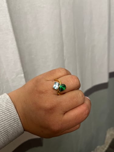 Close-up of a customer's hand wearing the gold Navae Birthstone Ring with a square blue and a pear-shaped green stone.