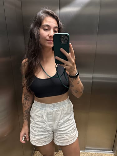 Cliente tirando uma selfie no espelho, mostrando sua case Nora Oliva com a alça para celular.