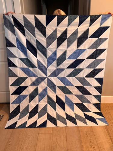Customer holds up their finished Nexus in Navy quilt, showing the blue and white geometric starburst pattern.