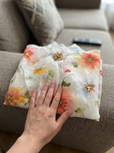 A customer's hand rests on their folded flower print blouse, showing the colorful and lightweight fabric on a couch.